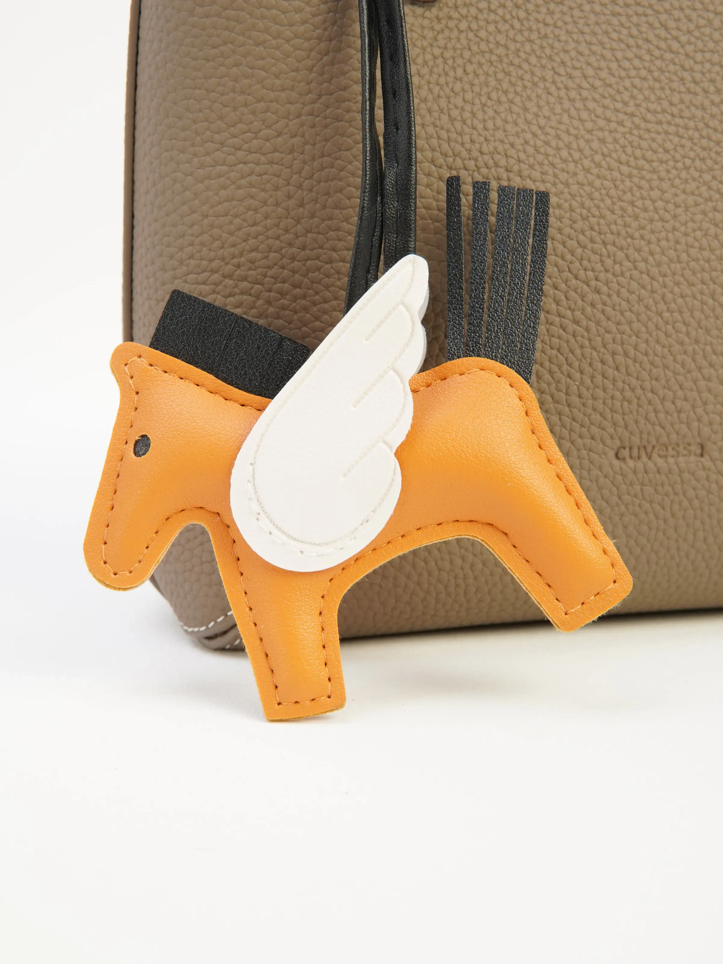 Close view of the orange horse-shaped charm styled with the Lena taupe tote